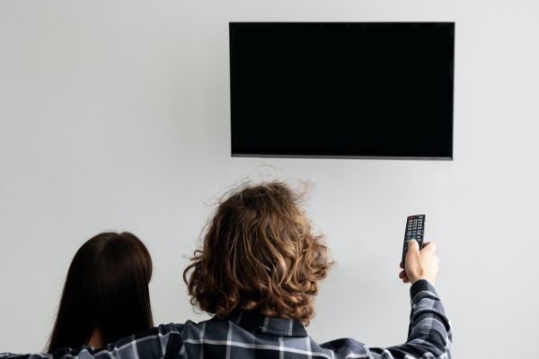 Couple Pointing Remote Control On Empty TV Screen Indoor, Back-View